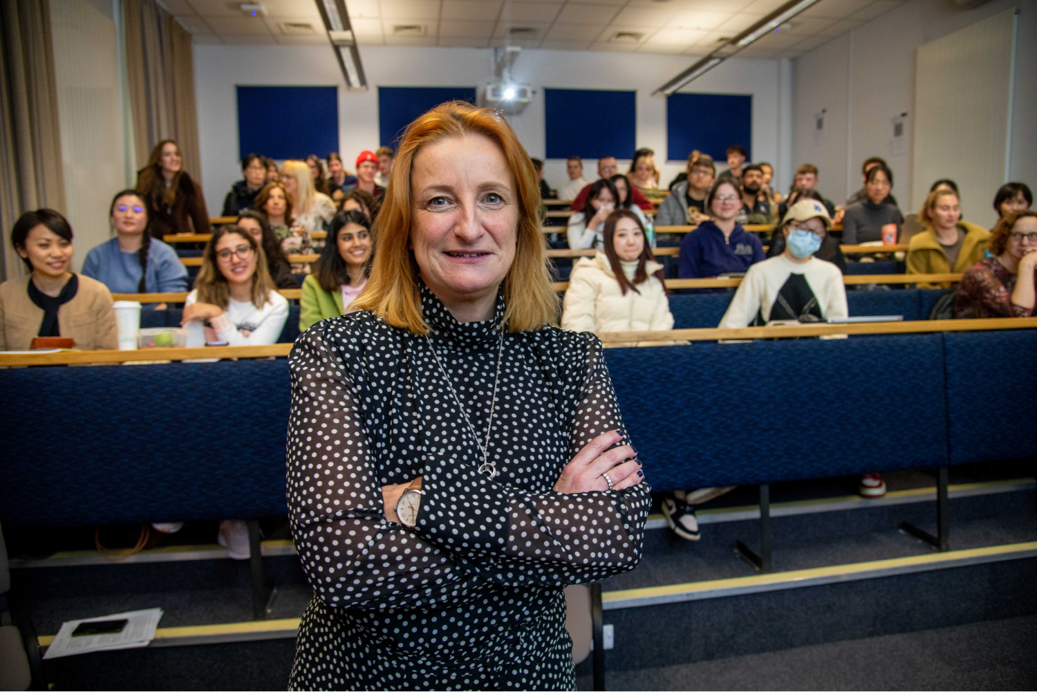 Alison Phillips stands before a full lecture hall with arms folded