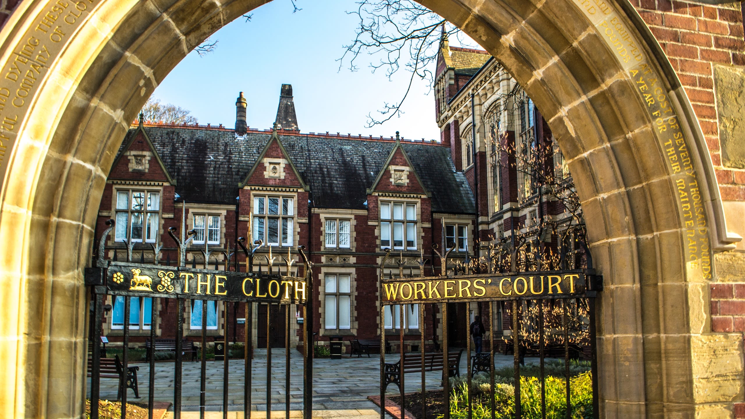 A Victorian red brick building behind an ornate iron gate that says 'The Clothworkers' Court' in gold text.