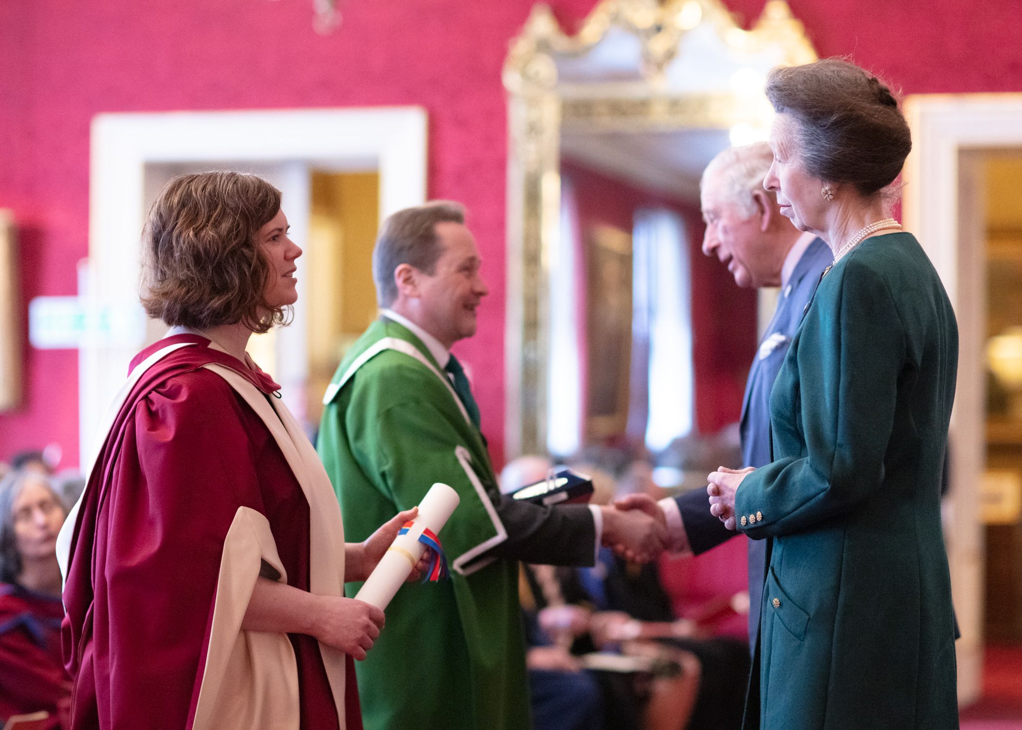Nick Plant and Amanda Maycock stand at the front of the ceremonial room and Prince Charles and Princess Anne present them with the Queen's Anniversary Prize