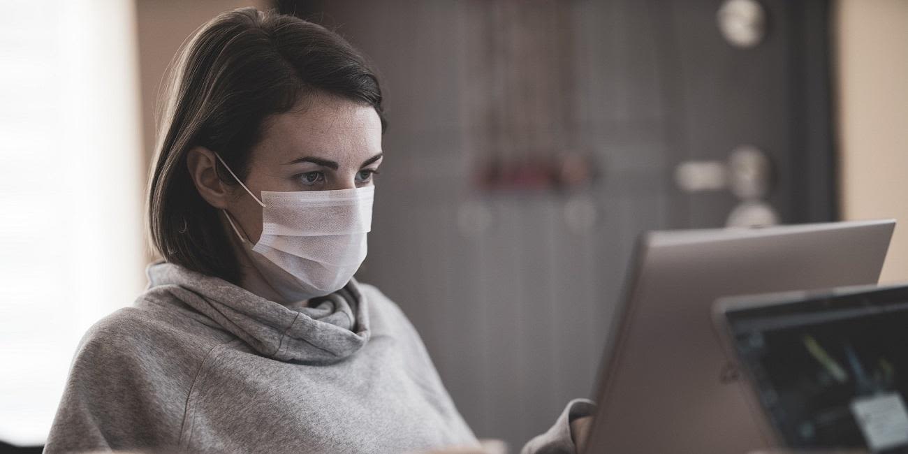 A woman wearing a mask sitting at a computer.