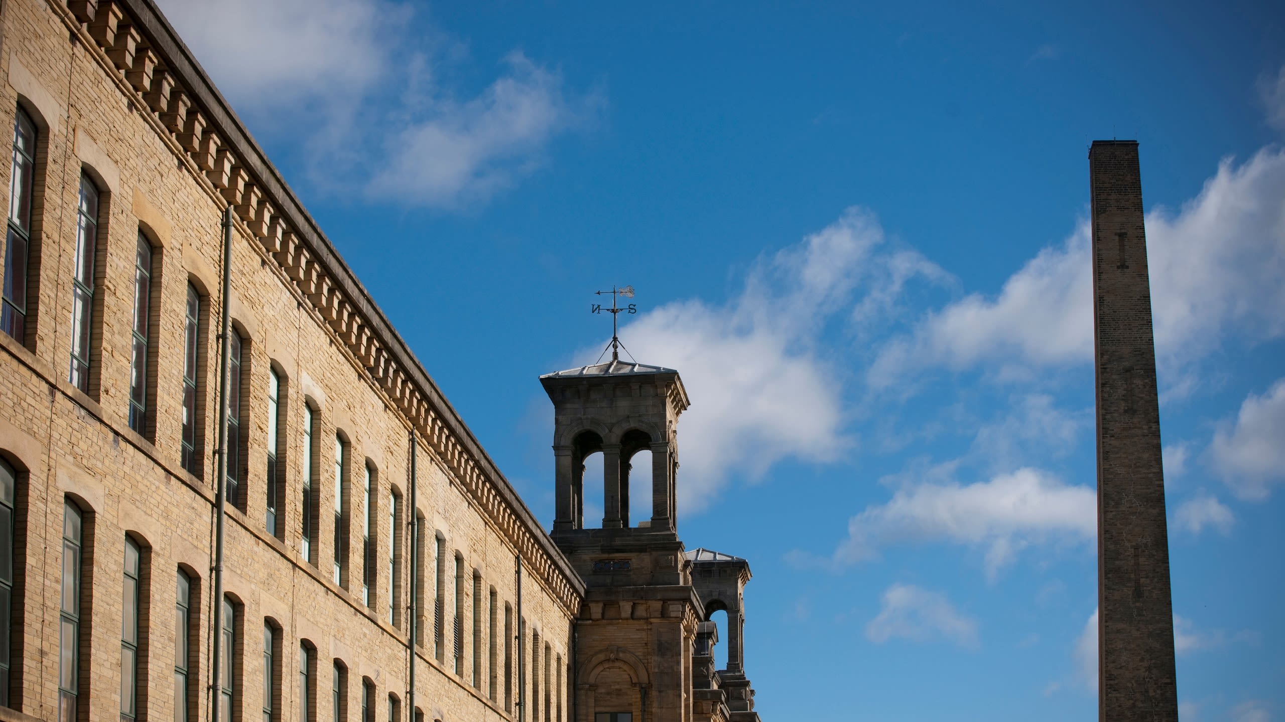 A grand Victorian mill building with two towers against a bright blue sky