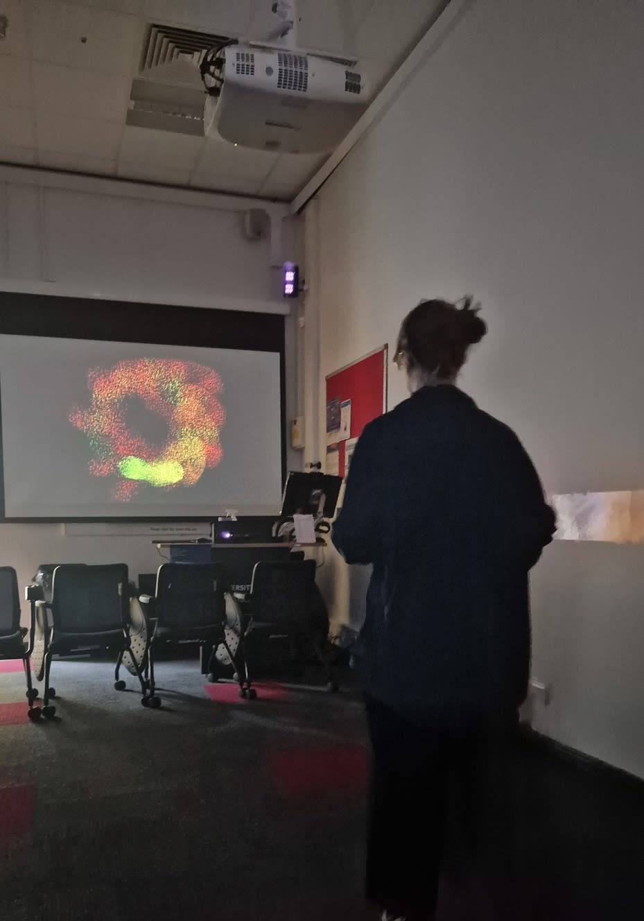A person in a darkened room, watching a screen with graphics on it