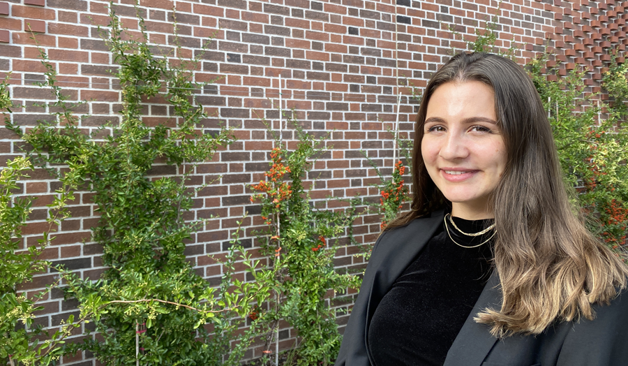 Lucy Cligg stood in front of a brick building wall with plants growing up it