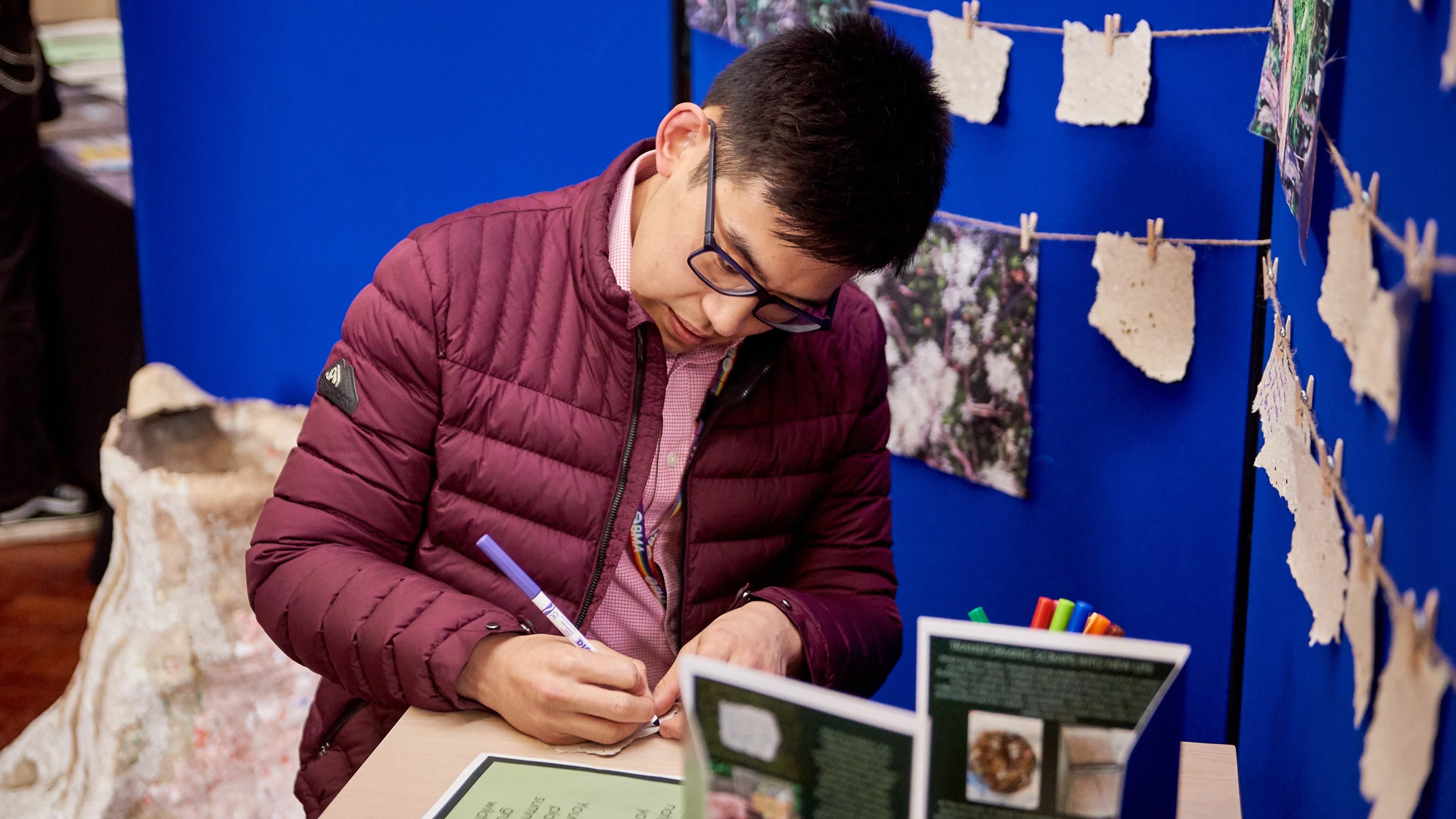 A person sat down with a display of handwritten notes pinned to a wall. They are writing a note to add to the wall.