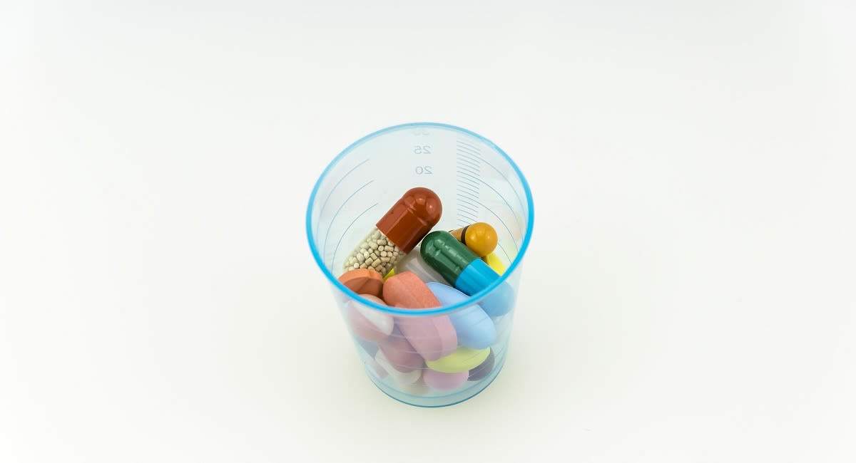A collection of multi coloured pills in a plastic cup.