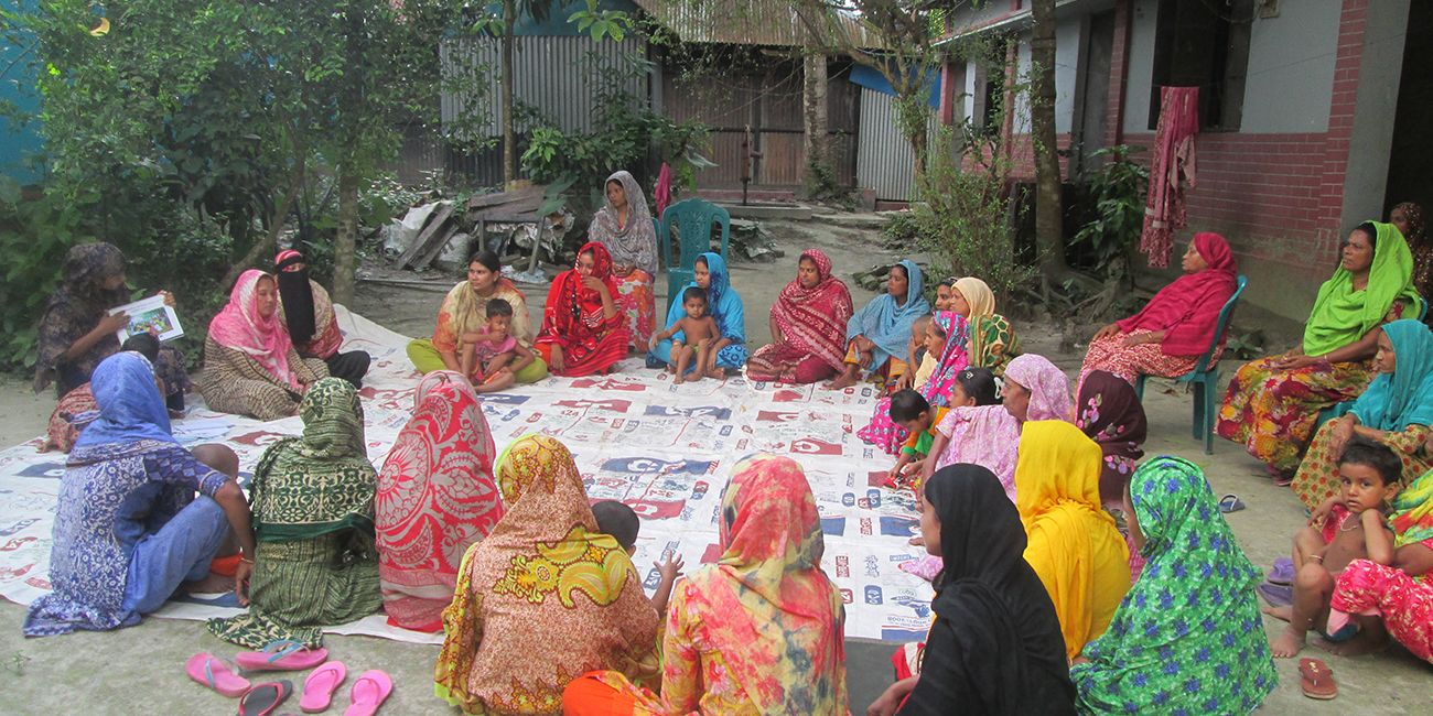 A group of Bangladeshi women and children sit in a circle.