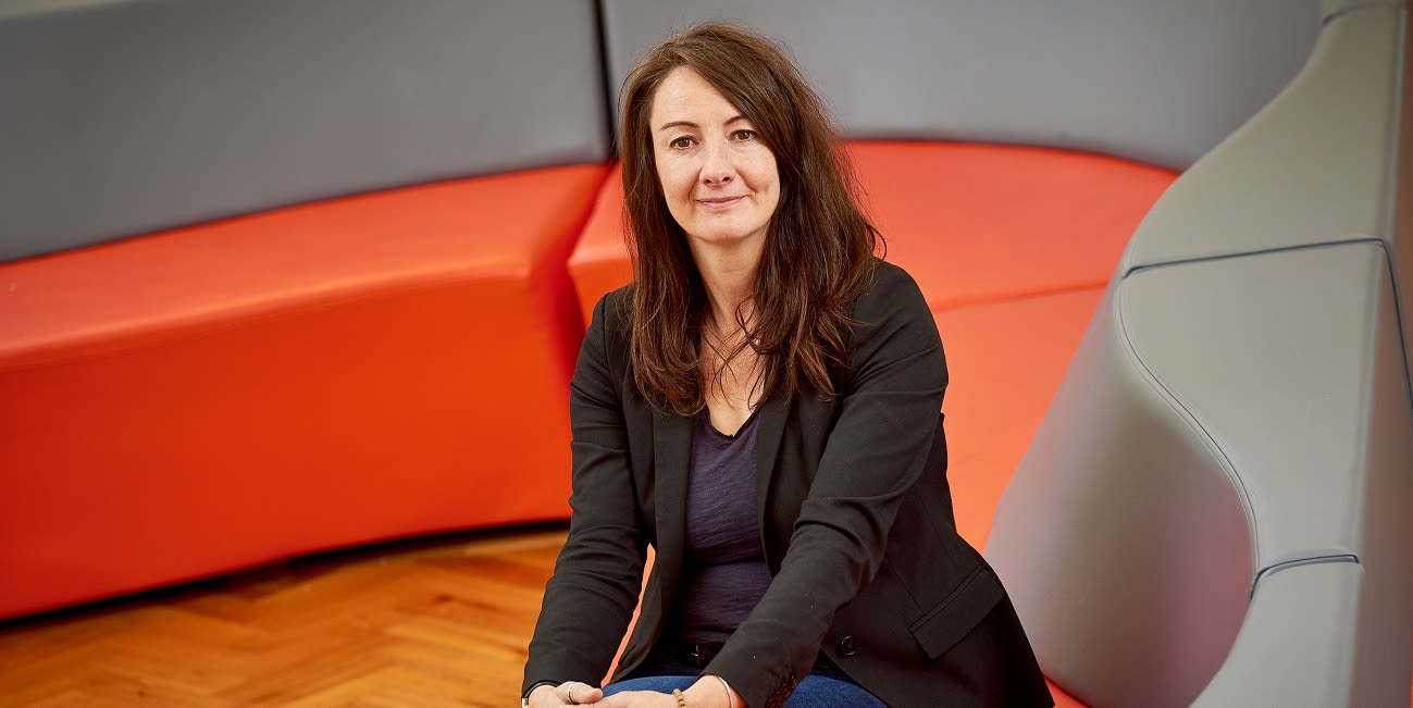 Dr Catherine Stones sits on a sofa and looks into camera.