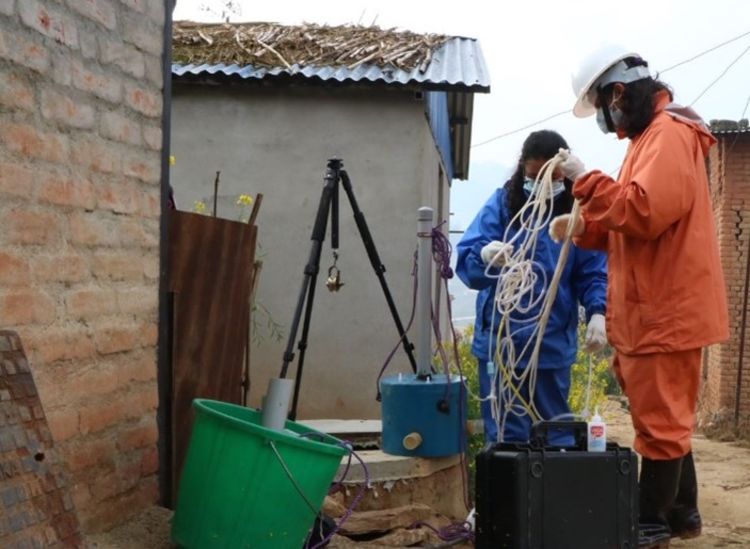two researchers wearing masks standing in a small yard preparing lengths of hose and wiring to set up an experiment.