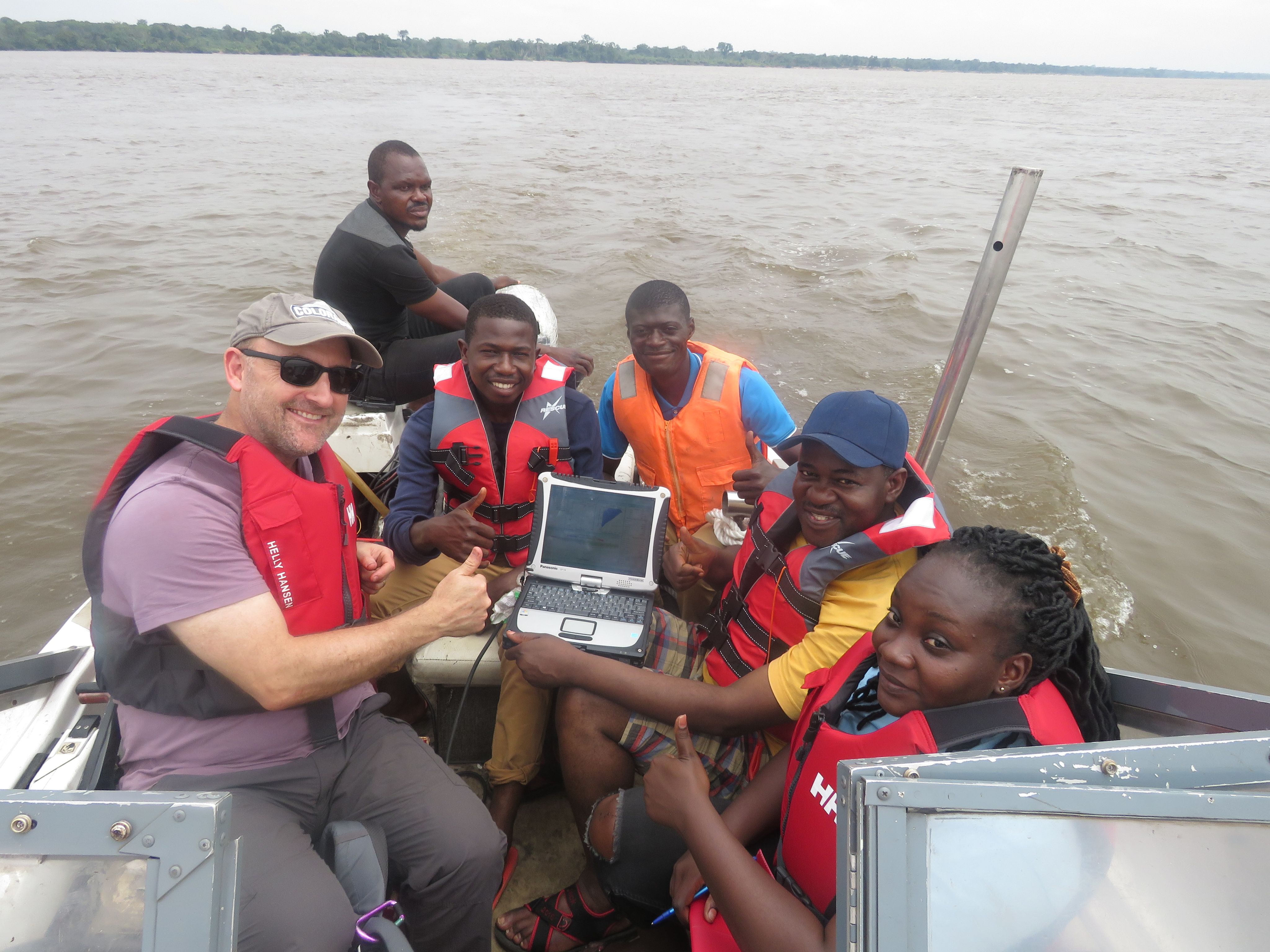 six researchers wearing safety jackets in a boat on a wide river.
