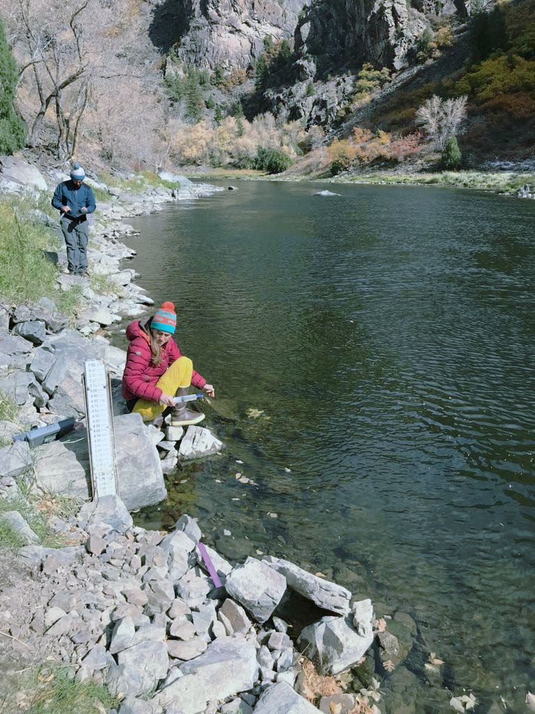 two researchers beside a river collecting water samples.