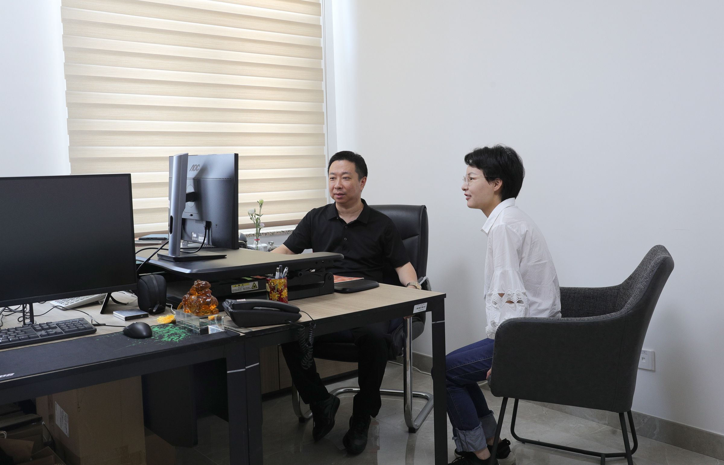 two people at a desk looking at a screen.