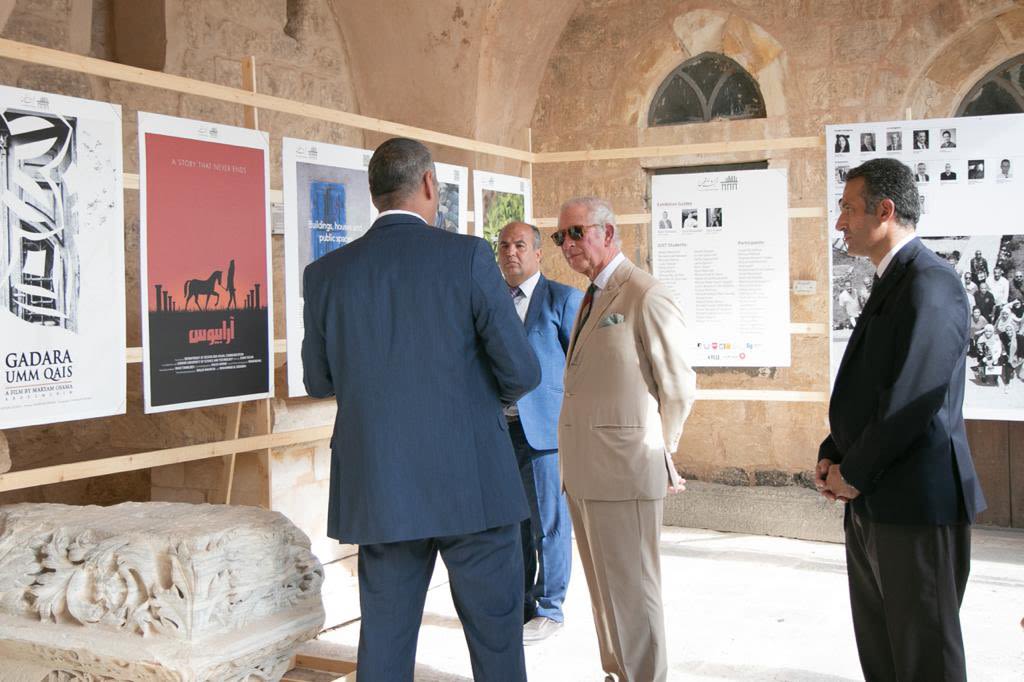 King Charles wearing a pale linen suit and sunglasses talking museum representatives.