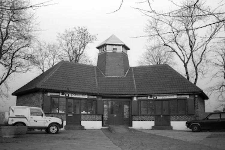 A black and white photo of The Pavilion Women's Photography Centre building. The sign on the building says 'Pavilion', there is a van parked outside and trees in the background.