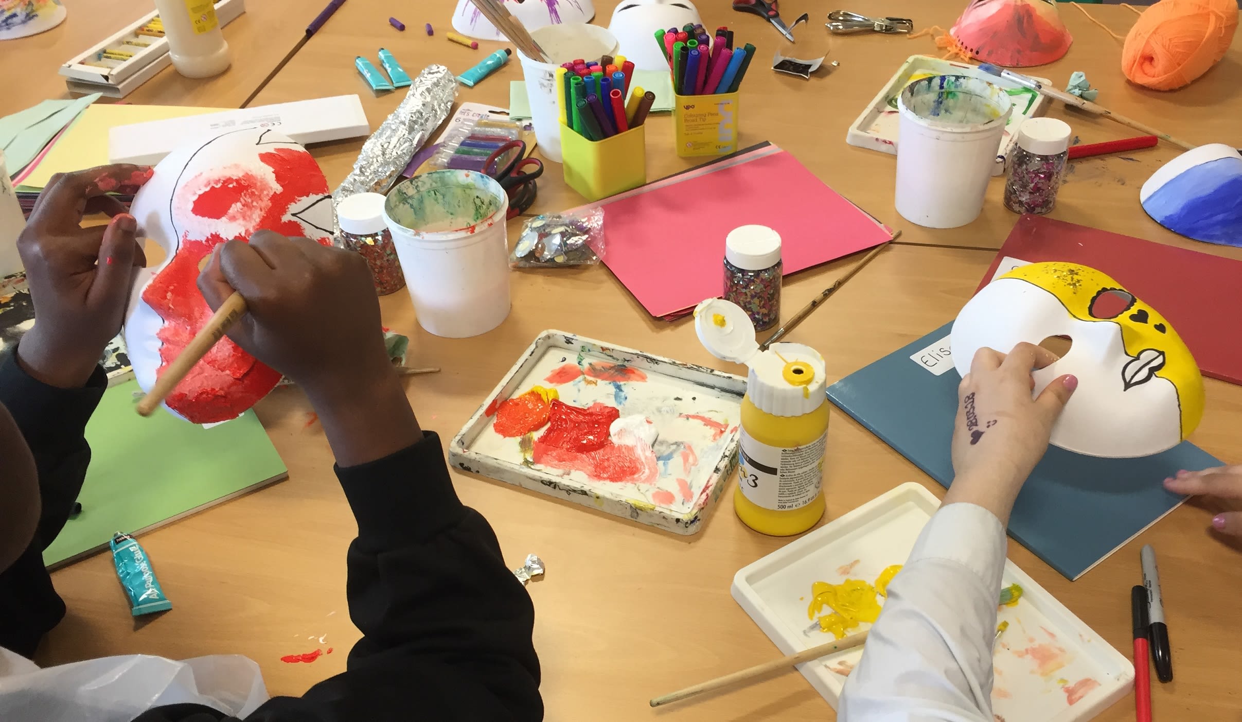 2 people sat at a table painting masks at the Art School for Rebel Girls