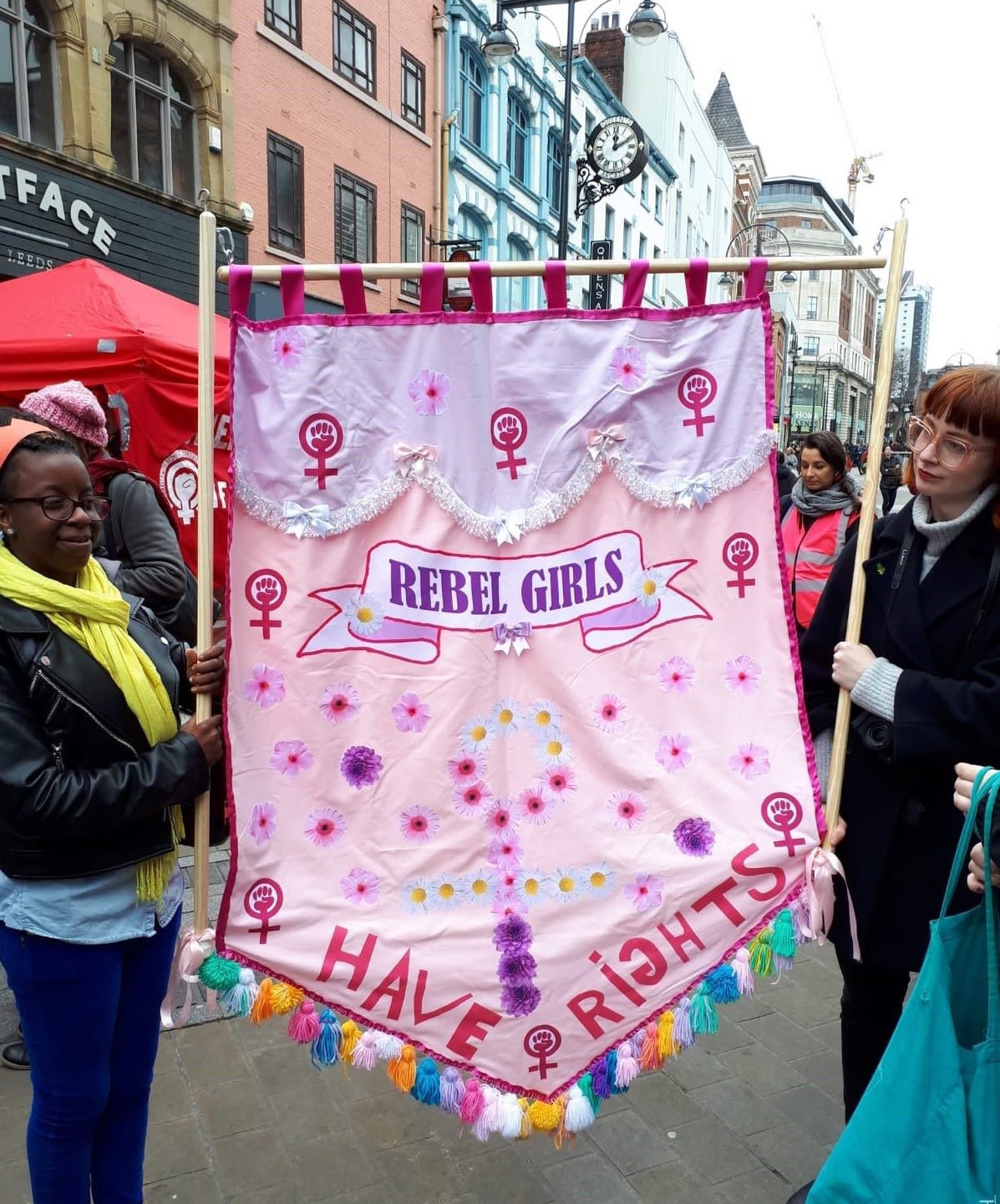 Two people standing in a street holding up a pink sign that says 'Rebel Girls have rights'.