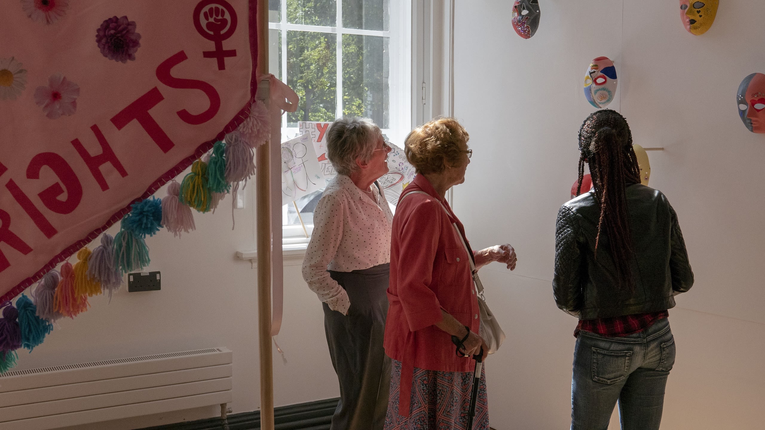 Three people looking at masks at an Art School for Rebel Girls art exhibition