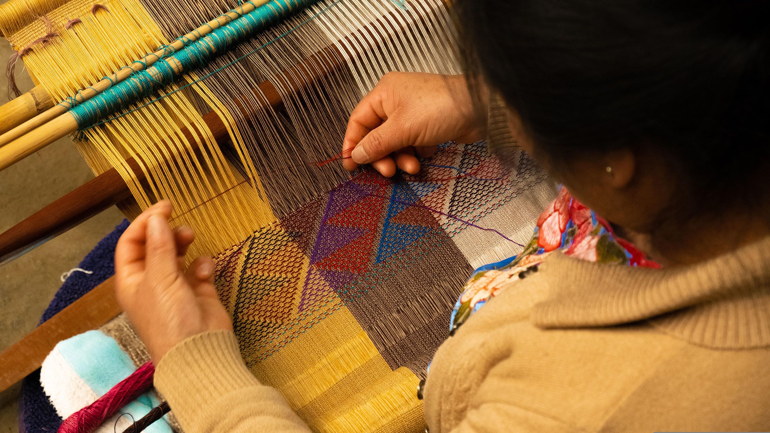 A close up of a person's hands as they weave colourful thread on a loom.
