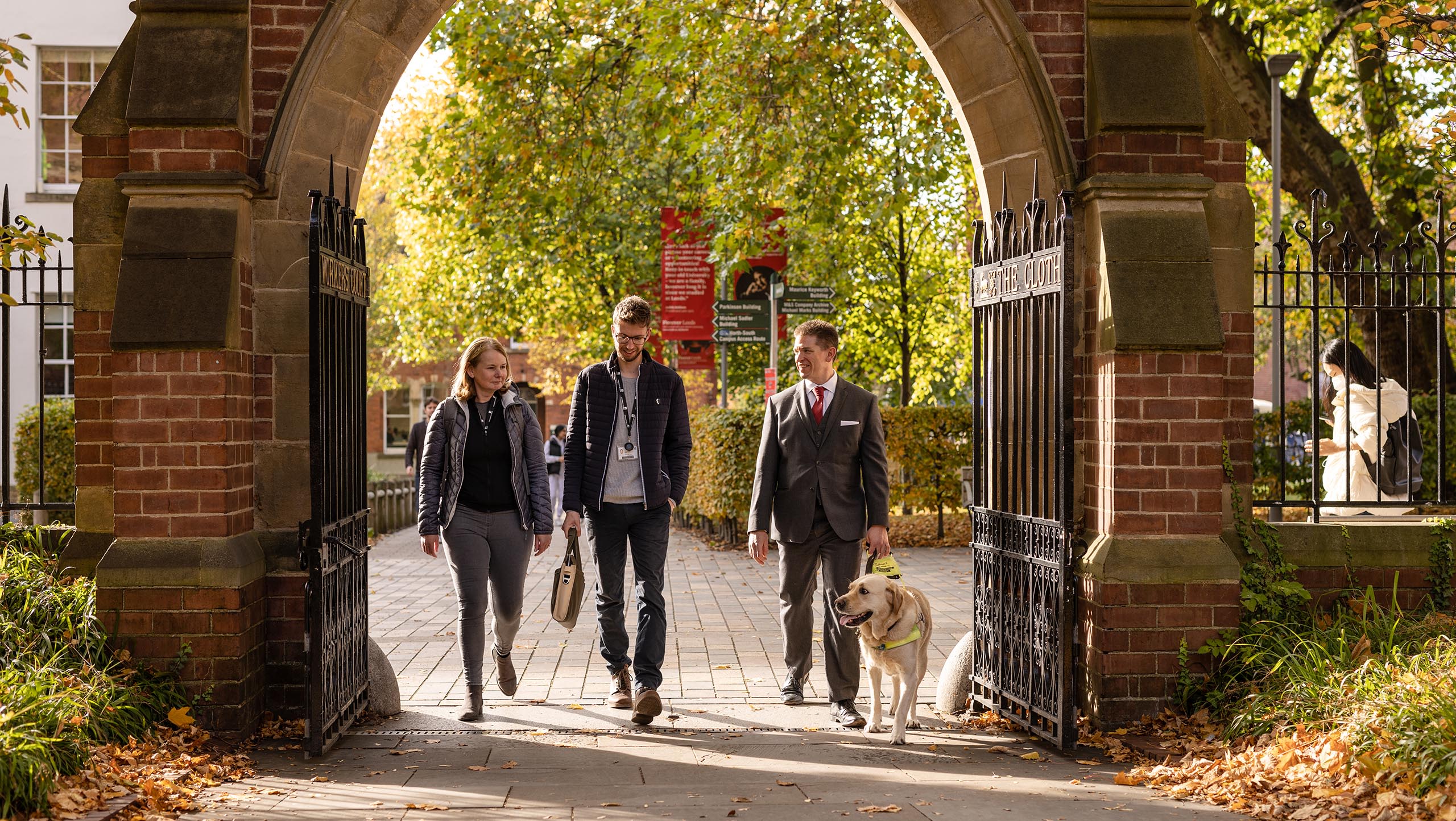 Three members of staff and a guide dog walking under Clothworkers' Court arch