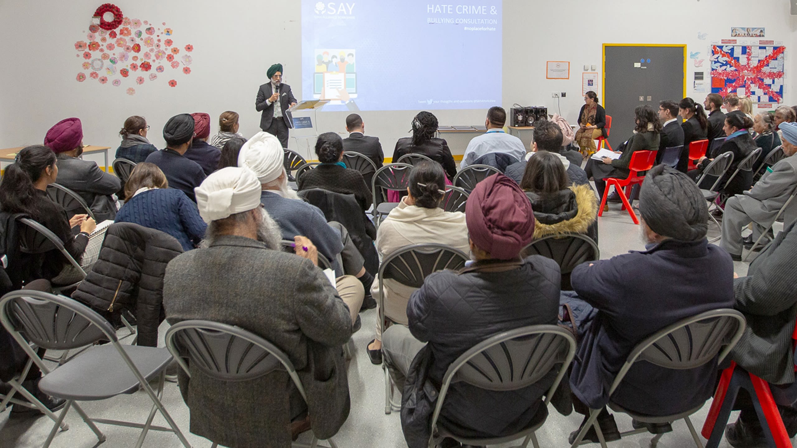 An audience listening to a speaker who is a Sikh and is giving a presentation