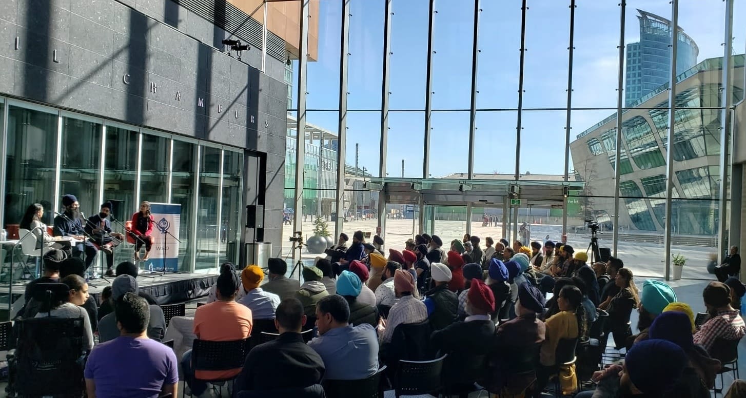 An audience listening to a talk being given by a small group of people in a large glass atrium