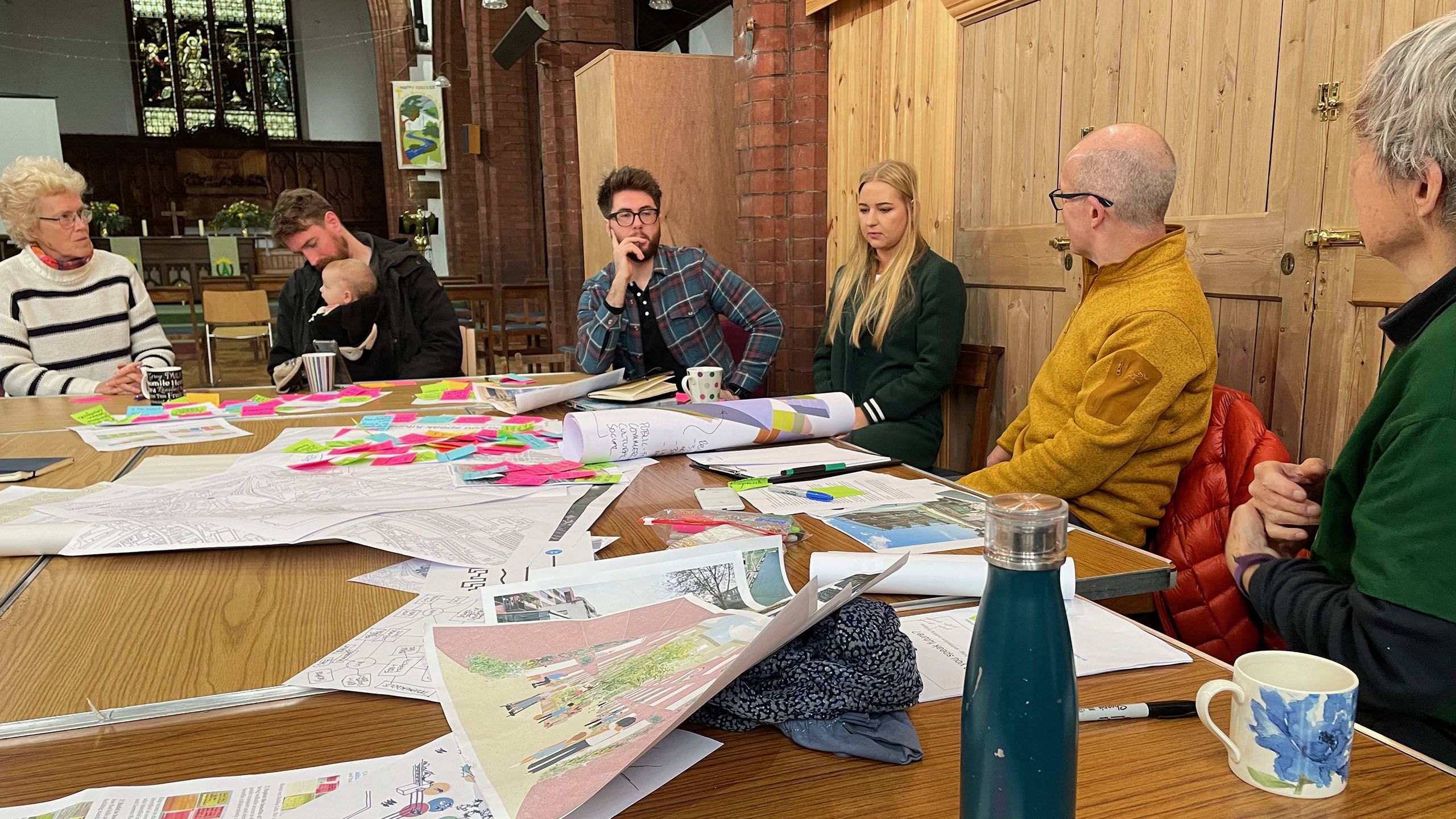 Several people sitting around a table having a discussion. The table is covered with images and post-it notes