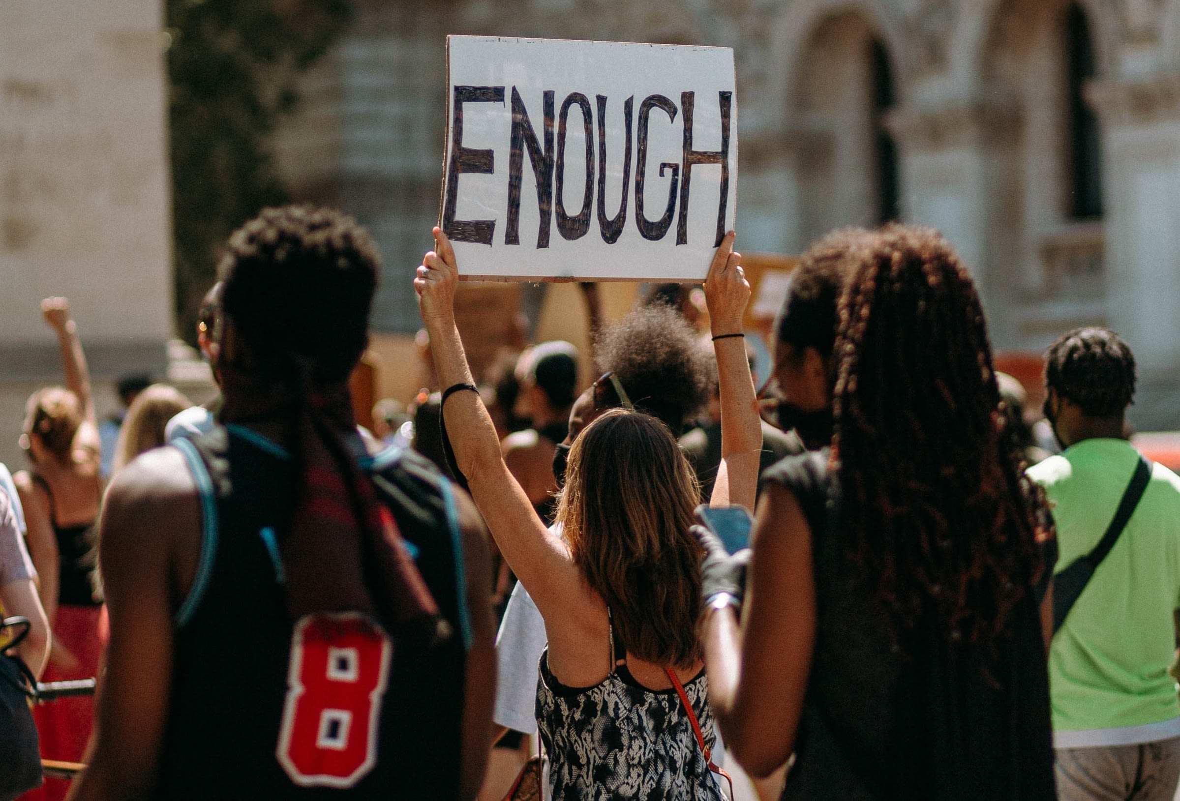 A crowd at a protest. One protestor holds a sign that reads 'Enough'