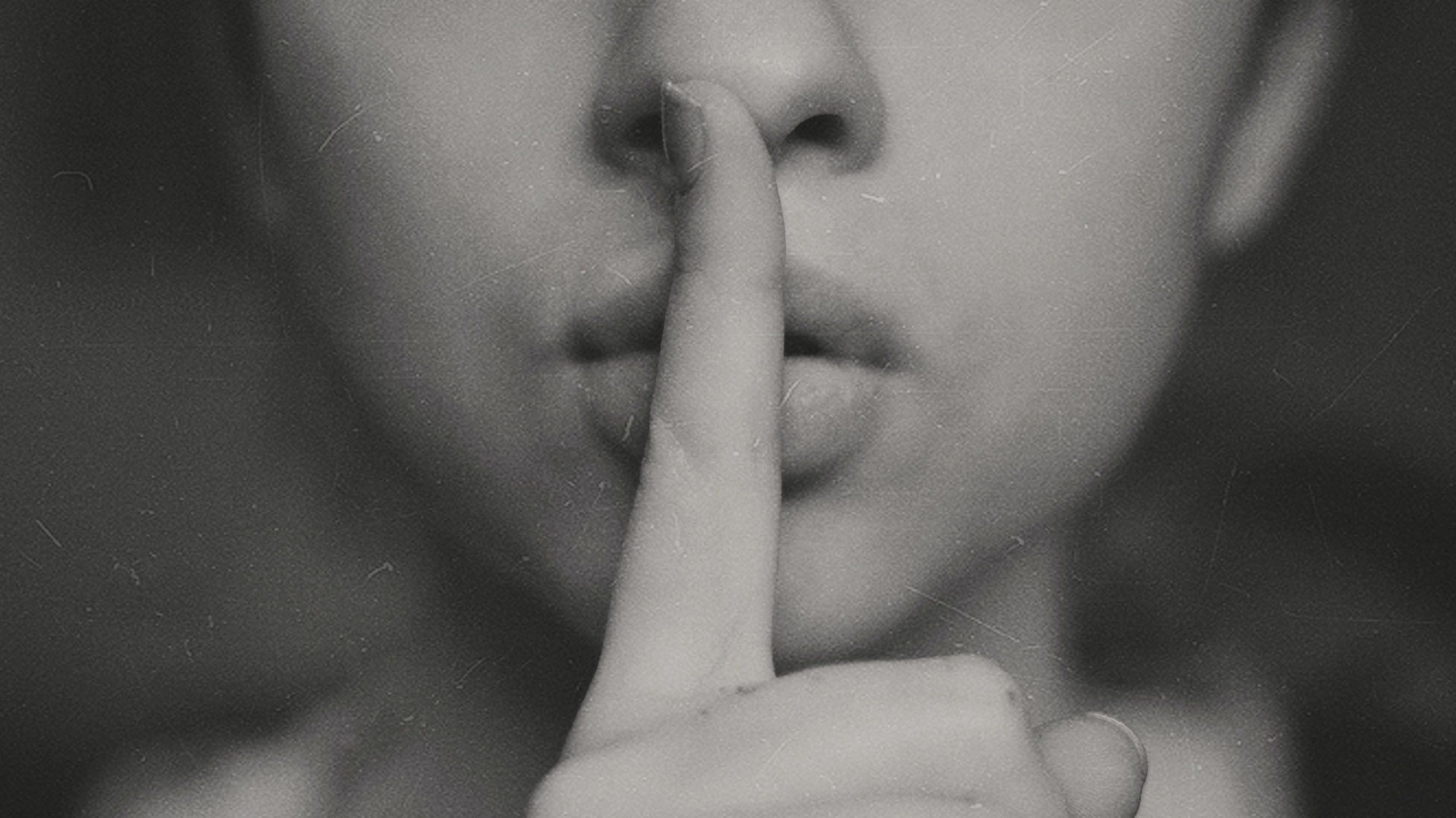 A close up of a person with one finger over their lips