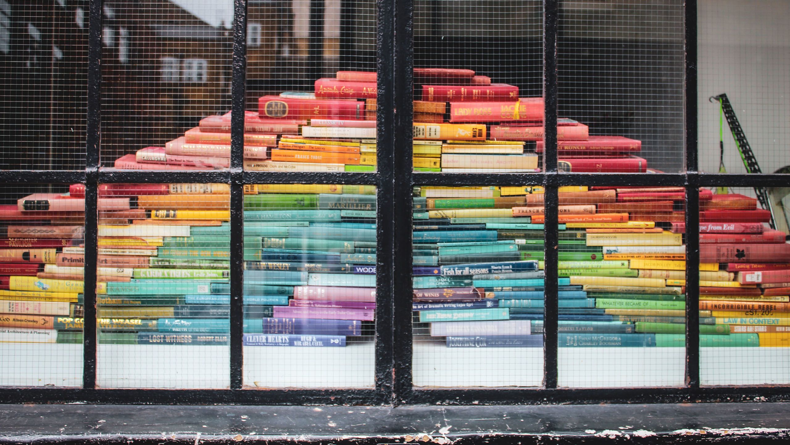 A large pile of rainbow coloured books behind a window