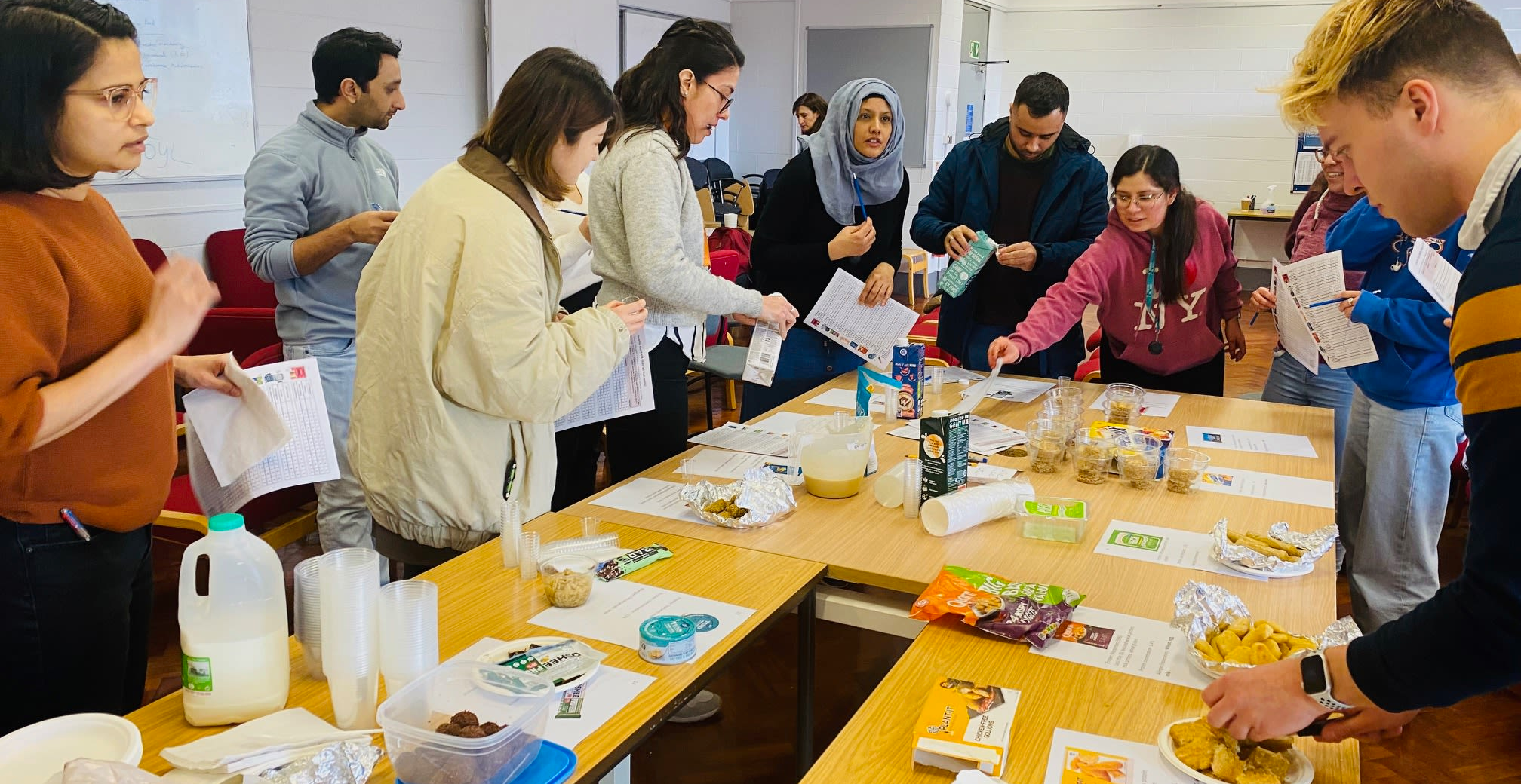 A group of people in a workshop, gathered around a large table, testing out and discussing meat-free products.