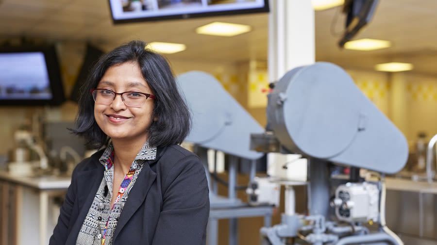 A smiling person in a food technology lab with equipment in the background.
