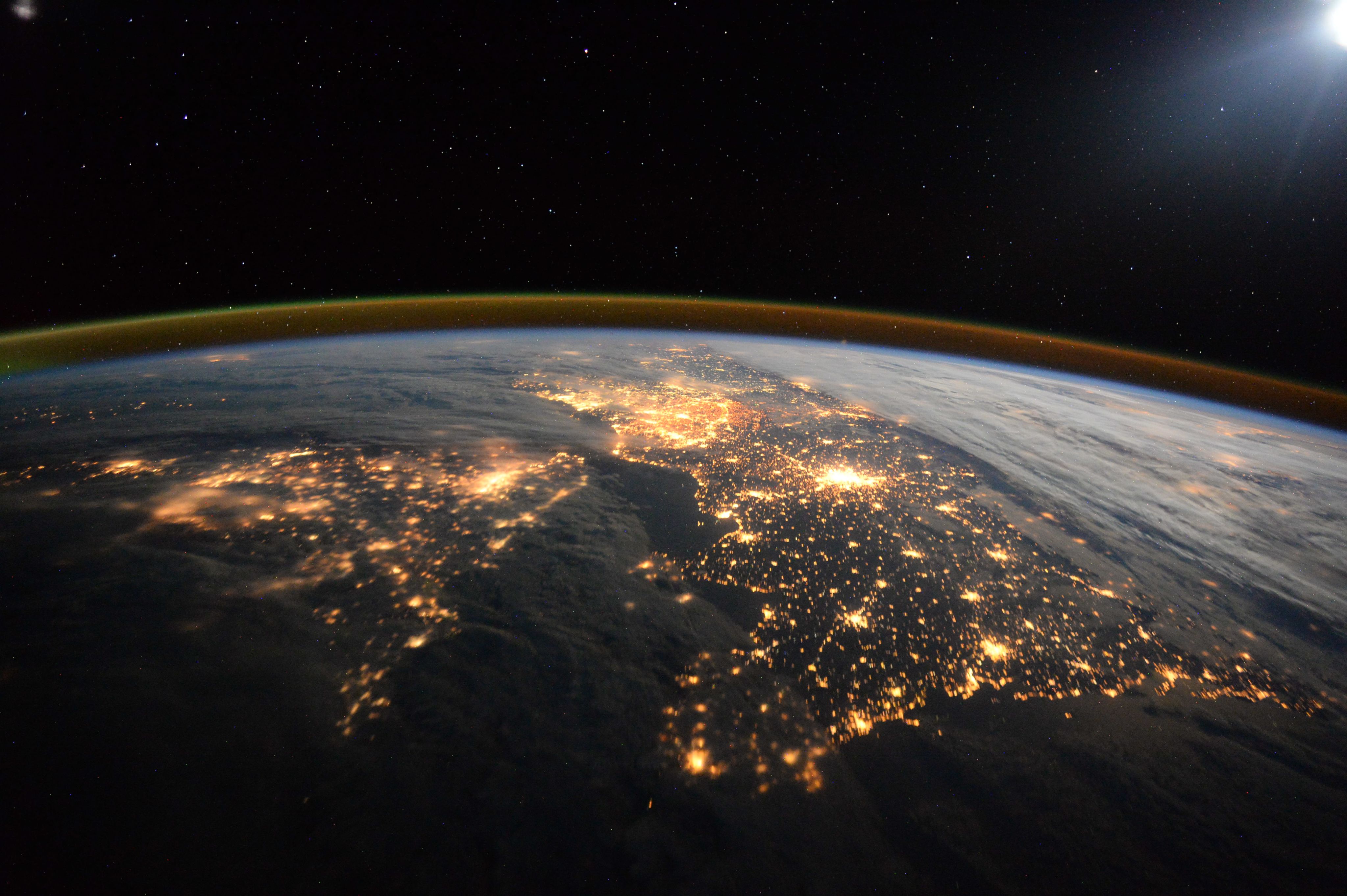 Satellite view of the UK and Northern France at night, with orange lights visible through clouds
