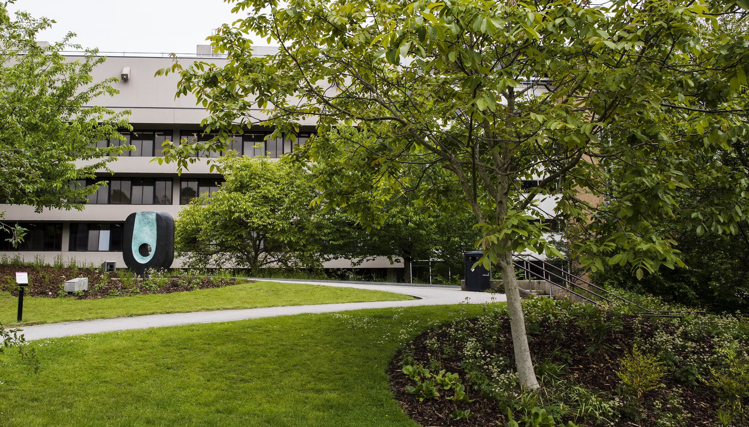 A path winds through grass and trees towards a Barbara Hepworth sculpture outside the Edward Boyle Library
